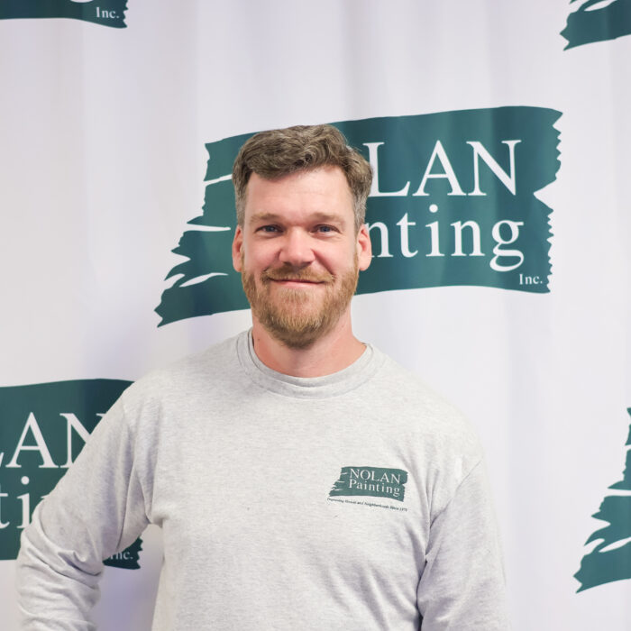 Portrait of a man with a beard and short hair, smiling, standing in front of a Nolan Painting backdrop.