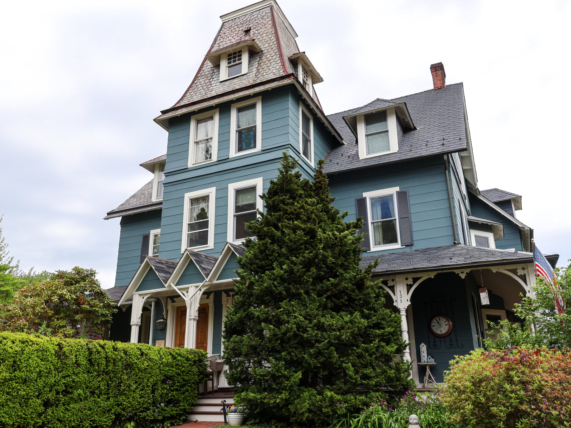 Blue Victorian house with a steep roof and turret, white-trimmed windows, and a lush front garden.