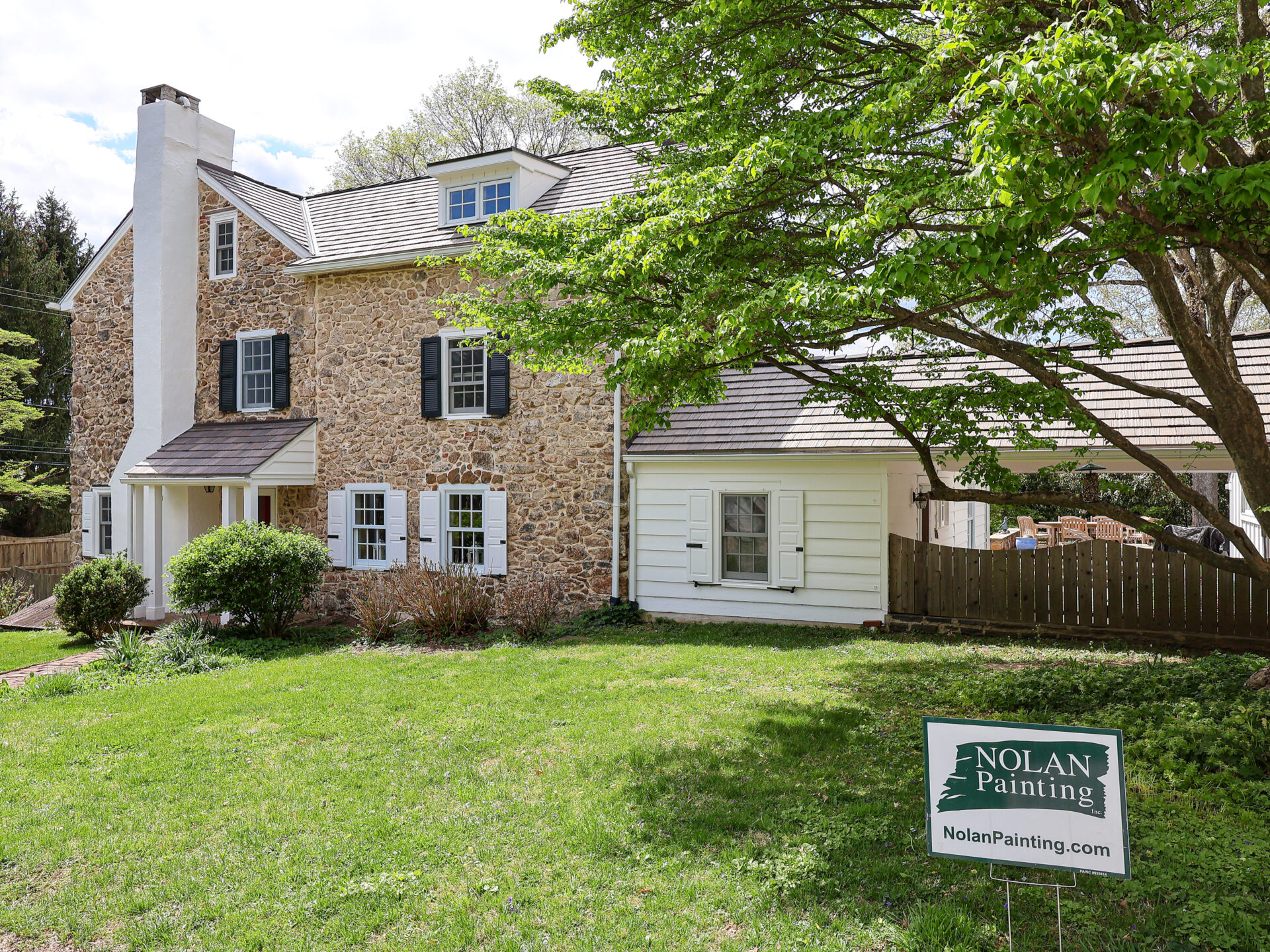 Stone house with white trim and shutters, green lawn, and a Nolan Painting sign in the front yard.
