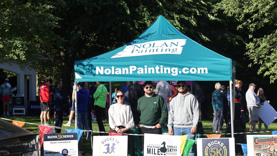 Teal Nolan Painting tent at an outdoor community event with people and race banners in the foreground.