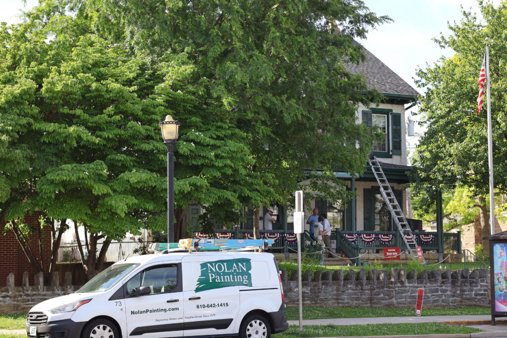 Painting company van in foreground with Nolan Painting logo, storefront with ladder and trees behind.