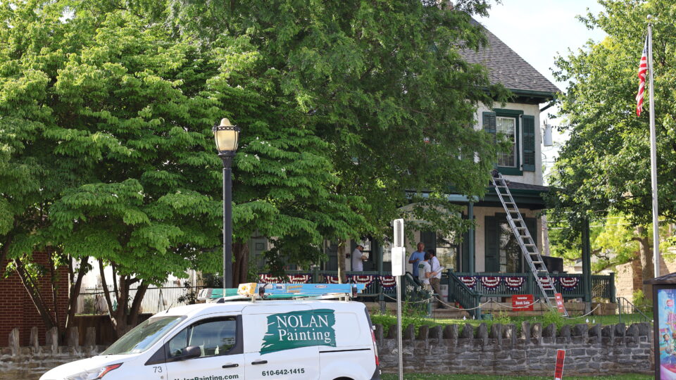 Painting company van in foreground with Nolan Painting logo, storefront with ladder and trees behind.