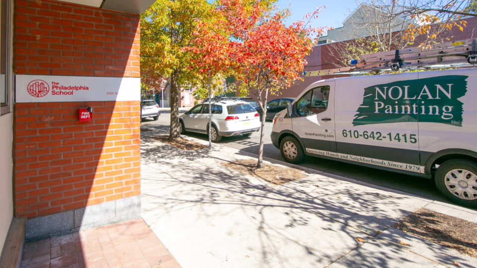 Brick building entrance with The Philadelphia School sign, a red Fire Dept box, and a Nolan Painting van under autumn trees.