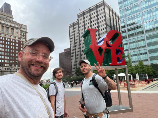 Group of friends taking a selfie in a city plaza with a colorful Love sculpture behind them behind them.