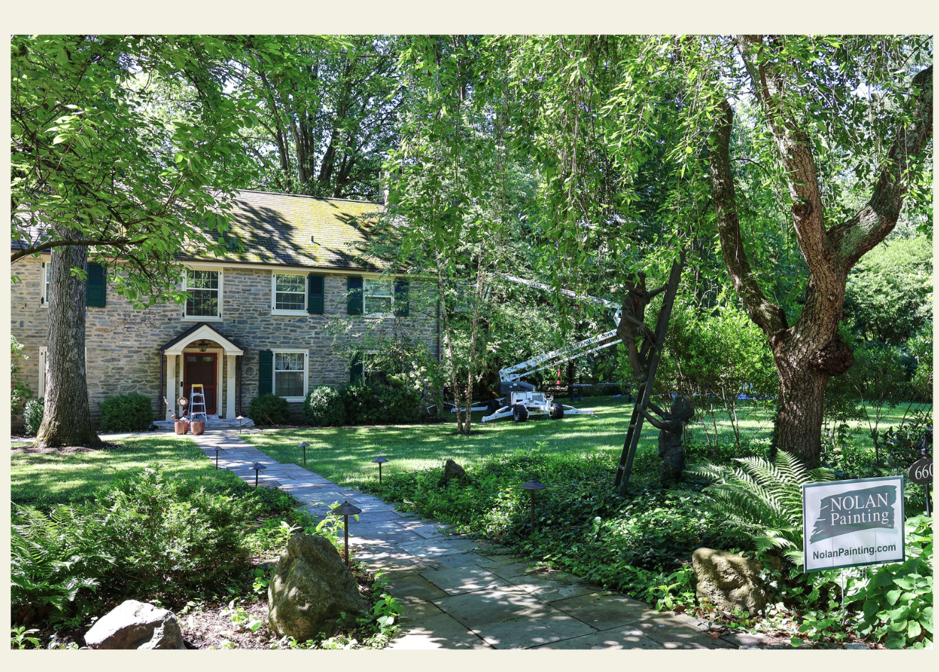 Stone-faced home with a front yard; a ladder and a painting crew crane are working on a tree near the house (Nolan Painting sign in foreground).