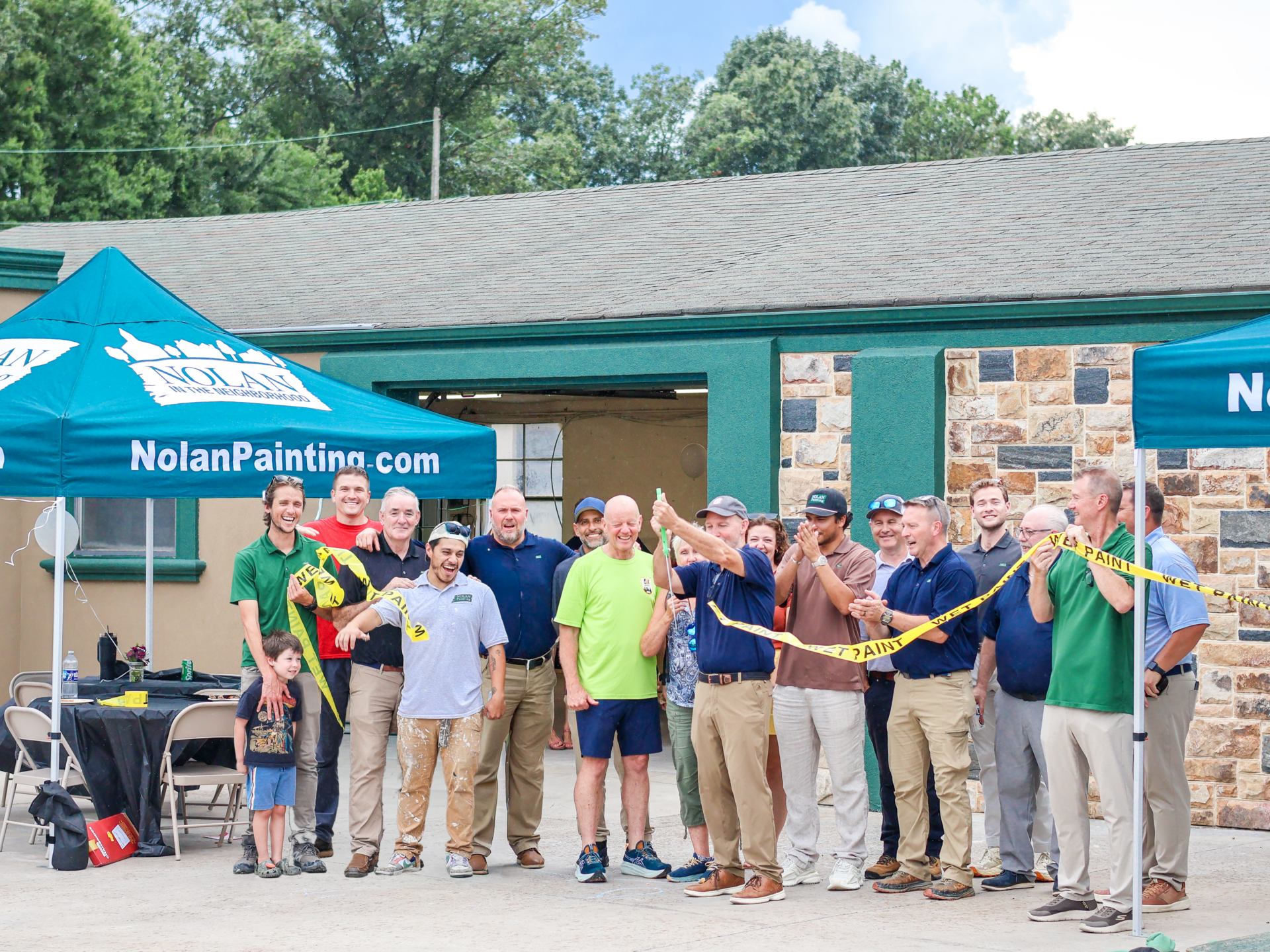 Group of people posing for a photo at an outdoor Nolan Painting event under blue tents.